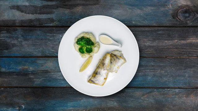 Pike perch fillet with broccoli and cauliflower Rotates on a plate. Beautiful wooden background. Top view