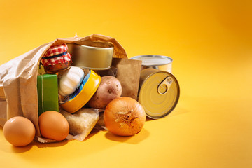 Various groceries inside paper bag on top of yellow background, with available copy space. Stockpiling food concept. - obrazy, fototapety, plakaty
