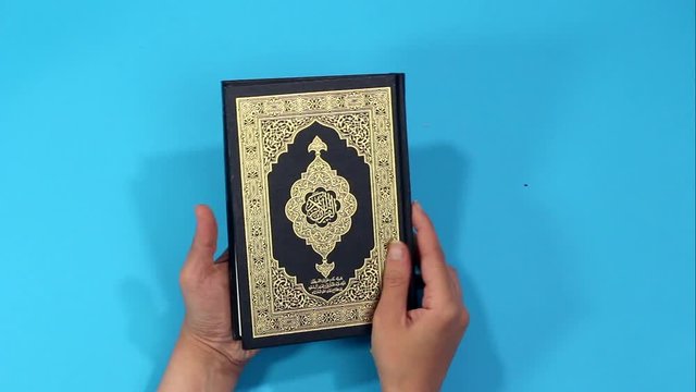 closeup hands holding Holy Quran with Arabic calligraphy meaning of Al Quran and is reading 