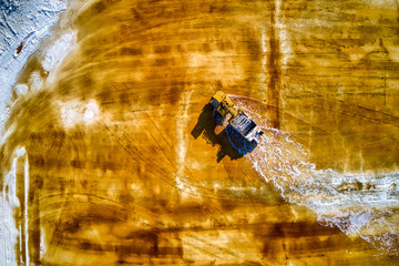 An aerial shot of a yellow salt truck mining for salt on a yellow salt lake. 