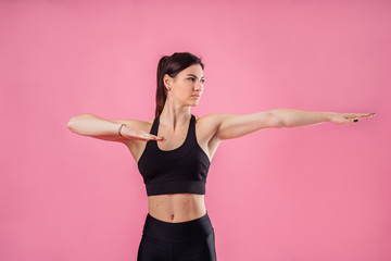 Fototapeta na wymiar Pumped up sports girl on a pink background in the studio does sports exercises with hands. Smiling and showing her high results by her muscular hands. Fitness for beginners - hands to the side