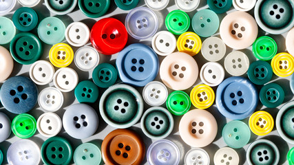 Fototapeta premium Colorful mixed sewing buttons lit by sunlight, flat lay. Items for sewing clothes. Top view