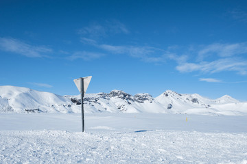 Snow covered road and traffic sign with mountains of Iceland in background