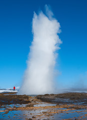 Fototapeta na wymiar Person in red jacket standing next to erupting Geysir Strokkur