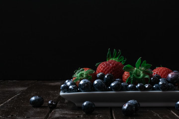 FRESH ORGANIC BLUEBERRIES AND STRAWBERRIES ON WOODEN TABLE AND BLACK BACKGROUND. DARK FOOD 