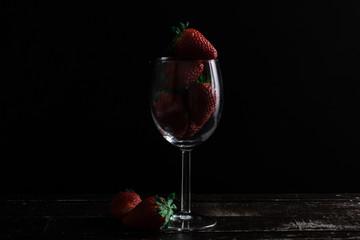 FRESH ORGANIC STRAWBERRIES IN A GLASS OF WINE ON WOODEN TABLE WITH BLACK BACKGROUND. DARK FOOD