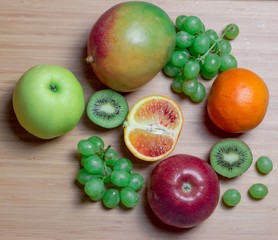 Fruits on a wooden table, sliced ​​orange and kiwi, green grapes, mango, red and green apples.