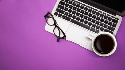 gray laptop with  cup of coffee and glasses on purple background table, working place at home or in the office