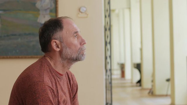 An elderly man looks thoughtfully at art objects sitting on a bench in a Museum