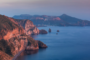 Coastline of island Lipari with view to volcan island Vulcano during sunset, cliffs and ocean, boats on water, Sicily Italy.