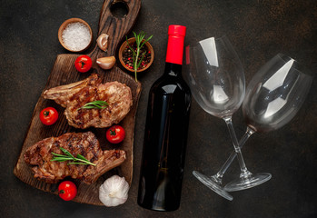 Dinner for two of grilled beef steaks and a bottle of wine and glasses on a stone background.