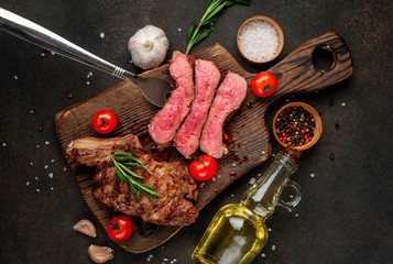 grilled beef steaks with spices, three slices of steak on a meat fork on a cutting board on a stone background