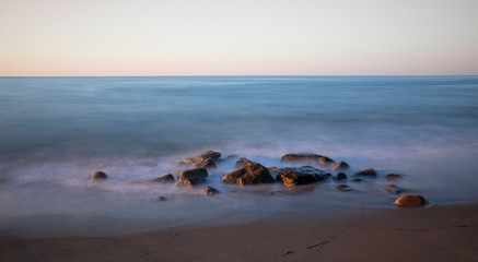 Fototapeta na wymiar Rocks with ocean waves on beach during sunset, Cefalu Sicily Italy.