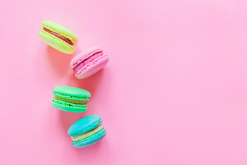 Sweet almond colorful pink blue yellow green macaron or macaroon dessert cake isolated on trendy pink pastel background. French sweet cookie. Minimal food bakery concept. Flat lay top view copy space.