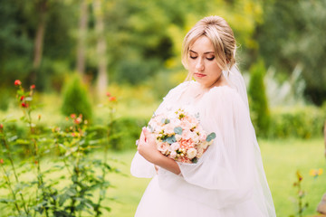 Portrait of a beautiful bride in a wedding dress and a luxurious bouquet of flowers from peony roses, festive makeup and hairstyle