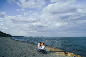 Lifestyle romantic evening for two. Young lovers went on a trip to the sea. Sitting on the sand in the evening sun and hugging, talking, kissing and enjoying the absence of people around.