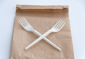 Stop using plastic. Plastic waste concept. Close up. Brown ecological paper bag and crossed plastic forks on it. Concept of Recycling plastic and ecology problem