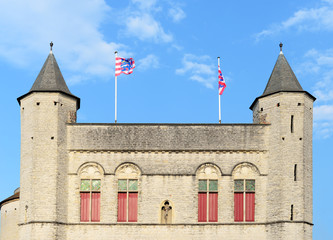Exit side of the Kruispoort (gate to Saint Cross) with flags of Bruges against blue sky with white fluffy clouds. One of the four remaining original entrance gates to the inner city of Bruges