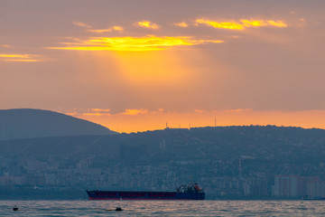Obraz premium Cargo ship sailing the sea at a golden sunset or sunrise. Ocean shipment across water as the sun sets or rises. Harmony and beauty in nature. Scenic peaceful sea view