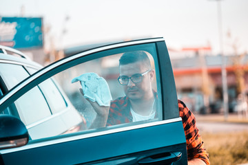 Young man leaning the windows on his car with microfiber cloth.