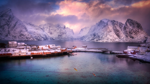 The Beautiful Nordic Coastal Village Of Reine, With Snowcapped Mountain, Pristine Fjord And Dramatic Sky.