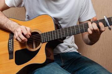 Fototapeta na wymiar A young European man without a face with jeans and a white T-shirt plays on an acoustic guitar
