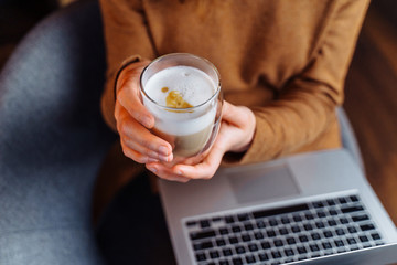A smart girl siting and working in the office with a laptop and a cup of aromatic espresso, cappuccino. Holding a laptop on her lap and enjoying a pleasant coffee aroma