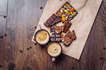 Two cups of espresso coffee with grains, craft bag and chocolate on a wooden table on a dark background. Top wiev.