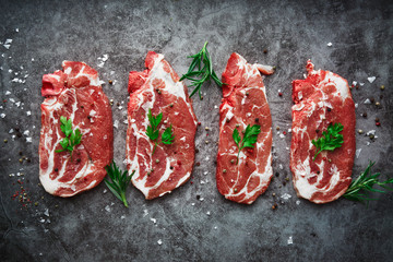 Four raw beef steaks with pepper, salt and rosemary on a dark background. Food concept.