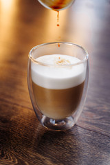 Close-up of a man’s hand pouring freshly brewed espresso in a coffee machine from a small paper cup into a transparent cup with whipped milk. Making a cappuccino or latte