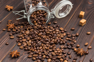 Cup of coffee, coffee beans sprinkled from glass jar on table. Spices star anise and pieces of...