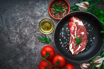 Raw beef steak with tomato, garlic, pepper, salt and rosemary on frying pan on a dark background. Food concept.