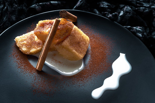 Traditional Spanish Dessert Of Fried Milk With Cinnamon And Decorated With Condensed Milk On Black Plate. Concept Of Food And Desserts.