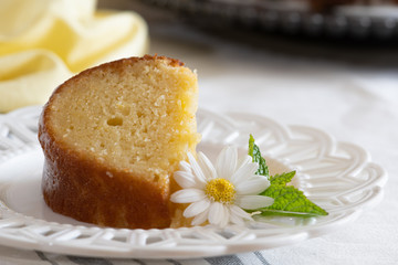 A slice of moist Lemon Ricotta Bundt Cake on a white decorative plate with a daisy and mint leaf garnish.