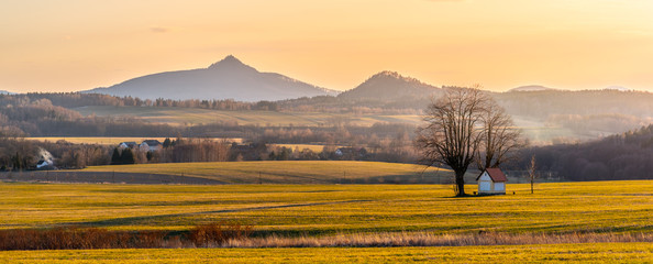 Hilly landscape illuminated by evening sunset. Green grass fields and hills on the horizont. Vivid...