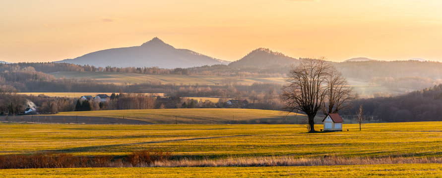 Hilly landscape illuminated by evening sunset. Green grass fields and hills on the horizont. Vivid spring rural countryside. Ralsko Mountain, Czech Republic © pyty