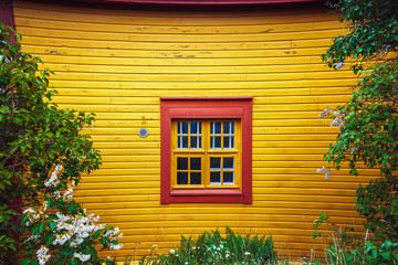 Fototapeta na wymiar Wooden window on a yellow wall. White window of a wooden house. Yellow wooden facade. Baltic design