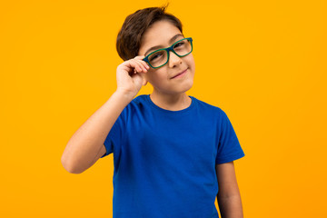 a boy in a blue t-shirt holds glasses with his hand and looks suspiciously at the camera on a...