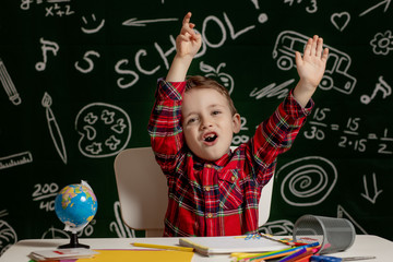 Emotional school boy sitting on the desk with many school supplies. First day of school. Kid boy from primary school. Back to school. Child from elementary school.