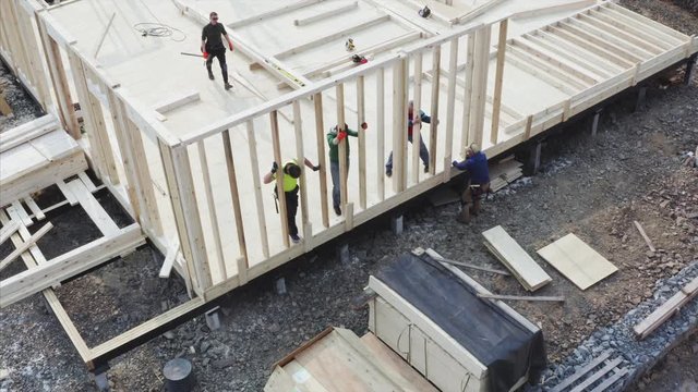 Aerial zooming out view of team of builders adjusting and moving the wall on the place. Frame house building site