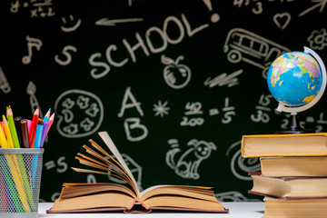 Back to school background with books, pencils and globe on white table on a green blackboard background.