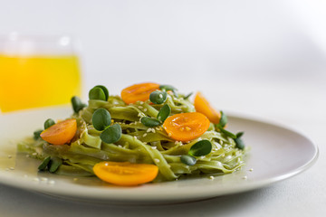 Green tagliatelle with olive oil, raw orange tomatoes, micro greens and sesame seeds with orange juice on the background. Horizontal close up. Copy space on the right.