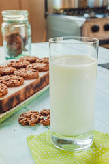 A glass of milk with chocolate cookies on the light green wooden table and a stove at kitchen