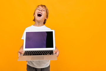 Naklejka premium Cute little boy in t-shirt and trousers holds a laptop isolated on yellow background
