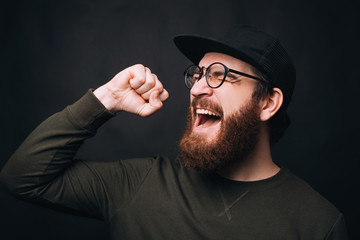Joyful man is screaming or singing because he won also he makes the winner gesture on black background.