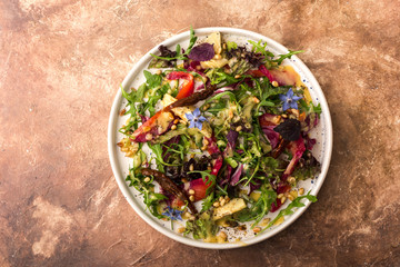Beautiful salad with mixed greens, sun dried tomato, pine nuts, artichokes and sauce in large white plate, top view