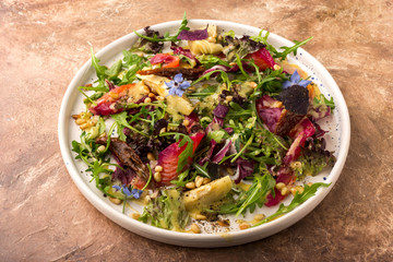 Beautiful salad with mixed greens, sun dried tomato, pine nuts, artichokes and sauce in large white plate, top view