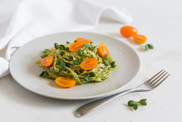 Green vegan healthy pasta with orange tomatoes and micro greens with white towel on the background and fork 