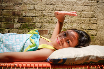 Cute Asian ethnicity little girl lying down on a bench, sunbathing in the morning at home. hand...