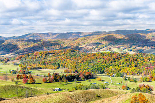 Autumn red colorful maple trees and mountains with farm houses on rolling hills above aerial high angle view landscape in Monterey and Blue Grass, Highland County, Virginia
